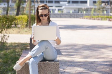 Bir dizüstü bilgisayar ile bir bankta genç kız.