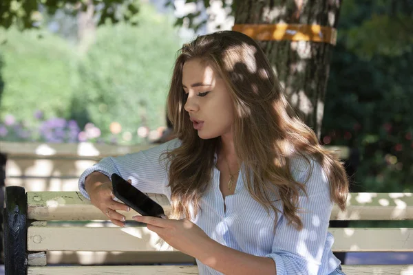 Junge schöne Frau sitzt auf Bank im Park. hübsches Mädchen an einem Sommertag im Freien. Hintergrund Natur Umwelt. — Stockfoto