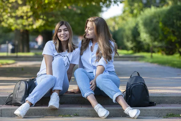 Två vackra unga flickor sitter på trappan. Flickvänner vilar i staden på sommaren. — Stockfoto