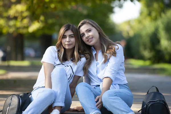 Två vackra unga flickor sitter på trappan. Flickvänner vilar i staden på sommaren. — Stockfoto