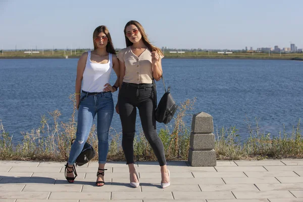 Zwei schöne junge und stilvolle Mädchen sitzen in einer Sommerstadt am Wasser — Stockfoto