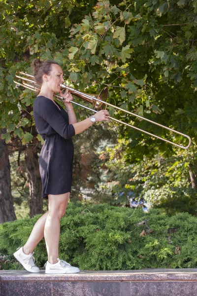Dívka se učí hrát na trombon. Dívka stojí na ulici městského parku. — Stock fotografie