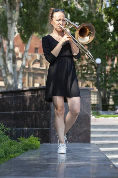 Dívka se učí hrát na trombon. Dívka stojí na ulici městského parku. — Stock fotografie