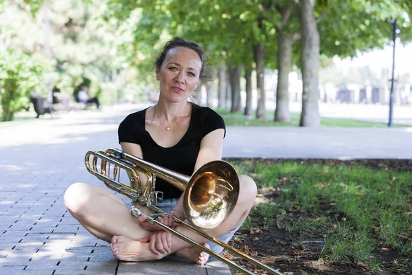 Dívka se učí hrát na trombon. Dívka hraje na deskách v parku. — Stock fotografie