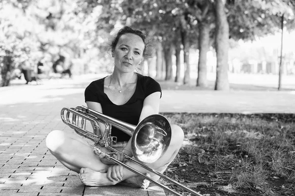 Dívka se učí hrát na trombon. Dívka hraje na deskách v parku. — Stock fotografie