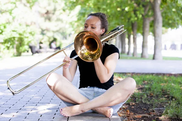 Dívka se učí hrát na trombon. Dívka hraje na deskách v parku. — Stock fotografie