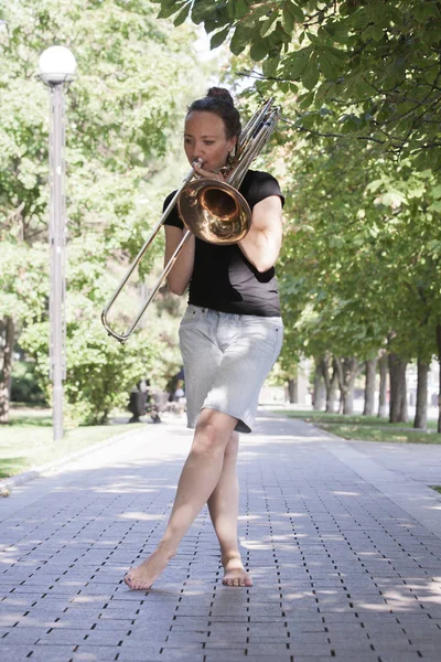 Dívka se učí hrát na trombon. Dívka stojí na ulici městského parku. — Stock fotografie