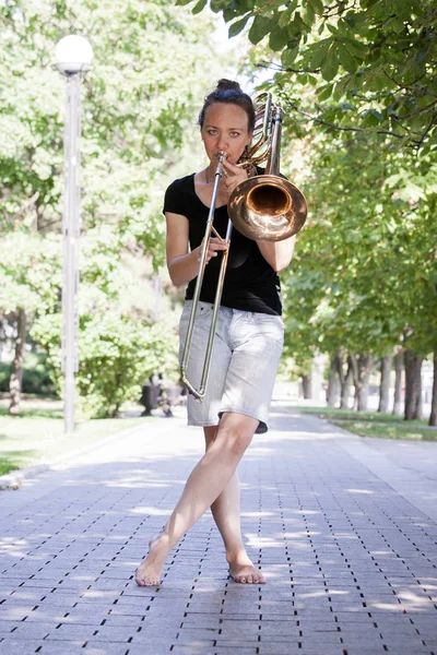 Dívka se učí hrát na trombon. Dívka stojí na ulici městského parku. — Stock fotografie