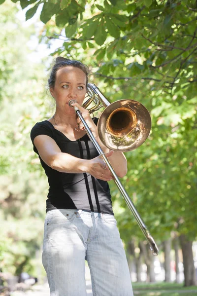 Dívka se učí hrát na trombon. Dívka stojí na ulici městského parku. — Stock fotografie