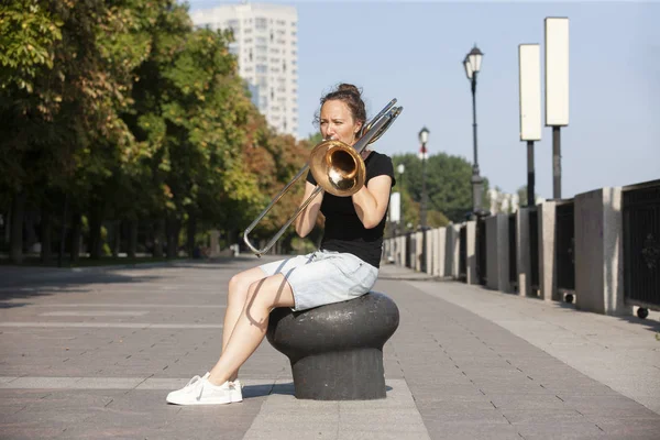 Une fille qui apprend à jouer du trombone. Fille joue assis sur la promenade . — Photo