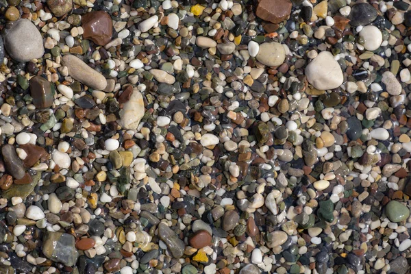 Dünner weißer Schaum und die vielen kleinen Blasen auf dem glitzernden Meerwasser mit den bunten Kieseln darunter — Stockfoto