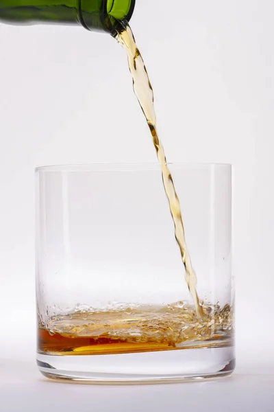 Närbild av ett elegant glas för sprit, med en spilld sprit, liknande rom eller whisky, på en vit bakgrund. — Stockfoto