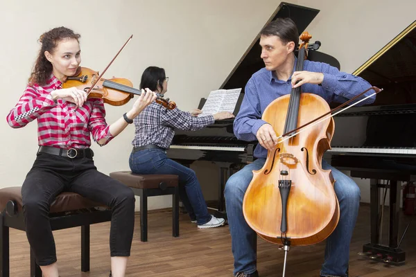 Family trio rehearsing. Father plays the cello, daughter is a violinist, mother plays the piano — Stock Photo, Image