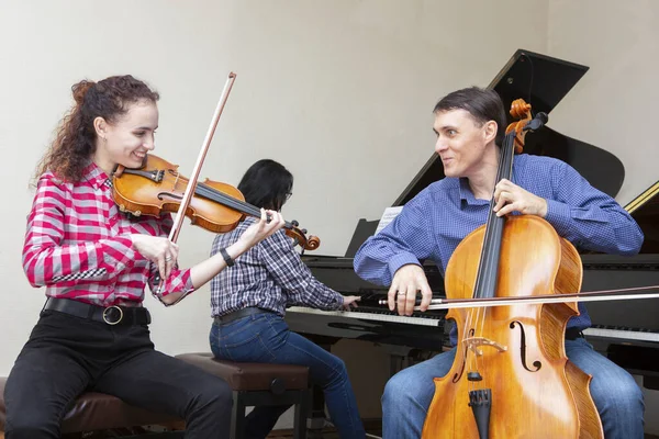 Trio familiar a ensaiar. Pai toca violoncelo, filha é violinista, mãe toca piano — Fotografia de Stock