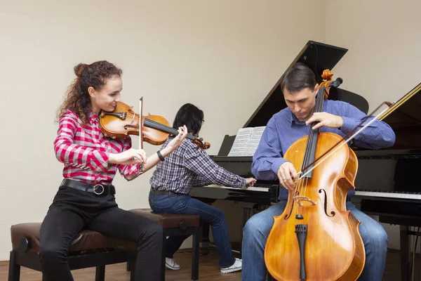 Trio familiar a ensaiar. Pai toca violoncelo, filha é violinista, mãe toca piano — Fotografia de Stock