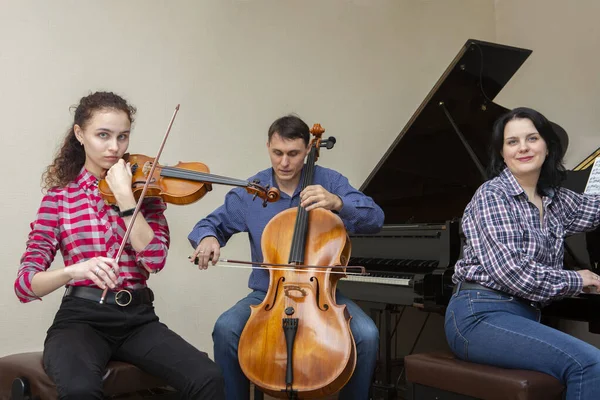 Trio familiar a ensaiar. Pai toca violoncelo, filha é violinista, mãe toca piano — Fotografia de Stock