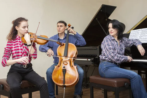 Familjetrion repeterar. Far spelar cello, dotter är violinist, mamma spelar piano — Stockfoto