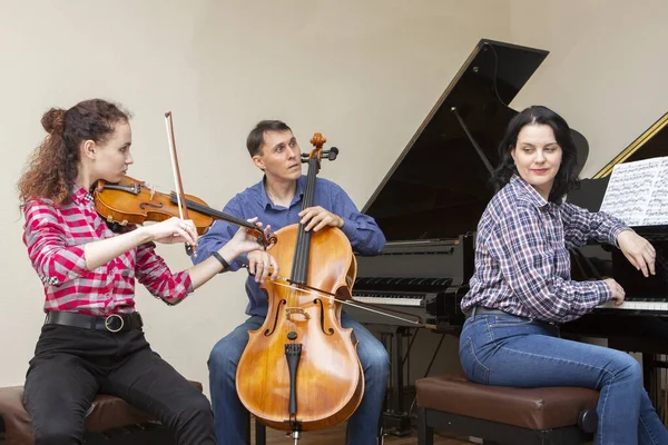 Trio familiar a ensaiar. Pai toca violoncelo, filha é violinista, mãe toca piano — Fotografia de Stock