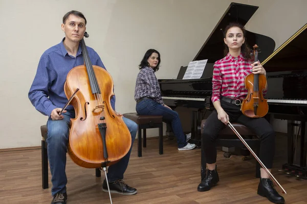 Familjetrion repeterar. Far spelar cello, dotter är violinist, mamma spelar piano Stockbild