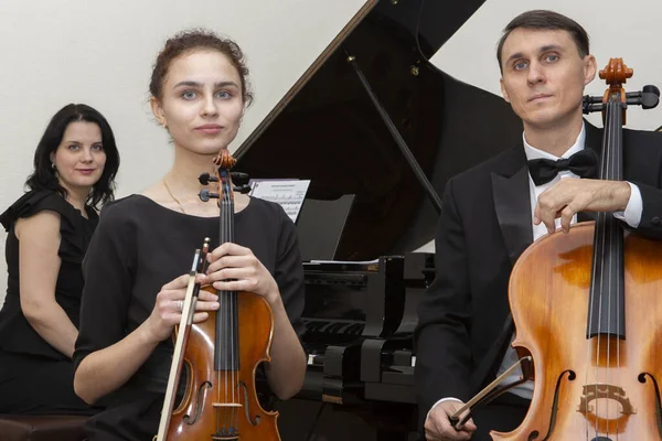 Familie muziek trio. Een jonge violist en cellist spelen, de pianist begeleidt hen. — Stockfoto