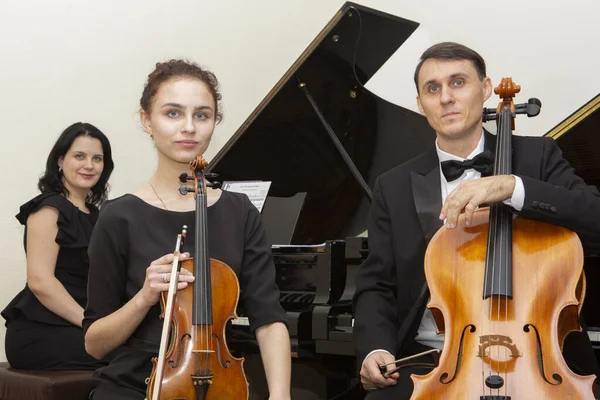 Familie muziek trio. Een jonge violist en cellist spelen, de pianist begeleidt hen. — Stockfoto