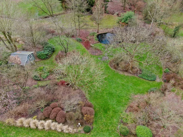 Aerial view of beautiful English garden type during winter season. Scenic View of a beautiful English style garden with a large green grass, little pound of water and small garden wood house.