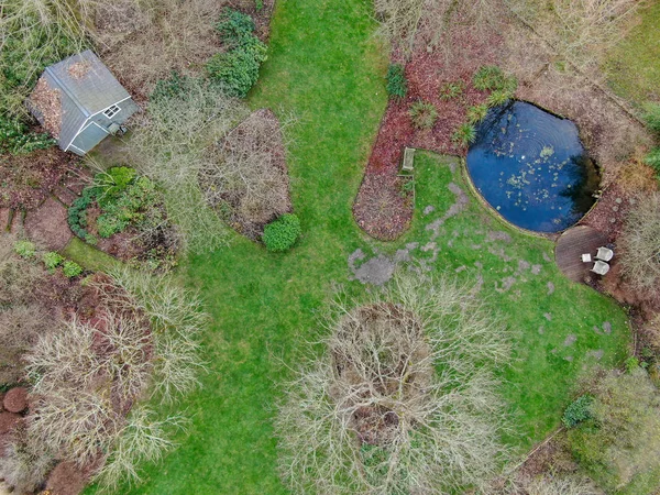 Aerial view of beautiful English garden type during winter season. Scenic View of a beautiful English style garden with a large green grass, little pound of water and small garden wood house.