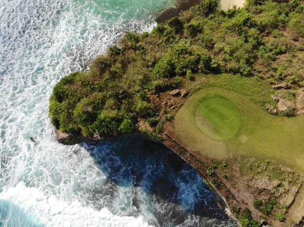 Aerial view of luxury golf field next the cliff, ocean and beach in Bali island, Indonesia. Aerial view of footpath on golf course.