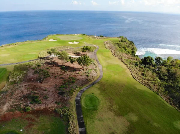 Aerial view of luxury golf field next the cliff, ocean and beach in Bali island, Indonesia. Aerial view of footpath on golf course.