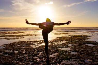 Gün batımında sahilde Yoga uygulamak sağlıklı kadın. Sahil günbatımında altında güçlü güven kadın. Kumsalda yoga yaparken genç kadın silüeti.