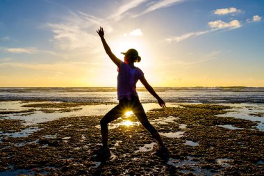 Gün batımında sahilde Yoga uygulamak sağlıklı kadın. Sahil günbatımında altında güçlü güven kadın. Kumsalda yoga yaparken genç kadın silüeti.