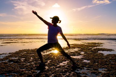 Gün batımında sahilde Yoga uygulamak sağlıklı kadın. Sahil günbatımında altında güçlü güven kadın. Kumsalda yoga yaparken genç kadın silüeti.