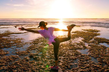 Gün batımında sahilde Yoga uygulamak sağlıklı kadın. Sahil günbatımında altında güçlü güven kadın. Kumsalda yoga yaparken genç kadın silüeti.