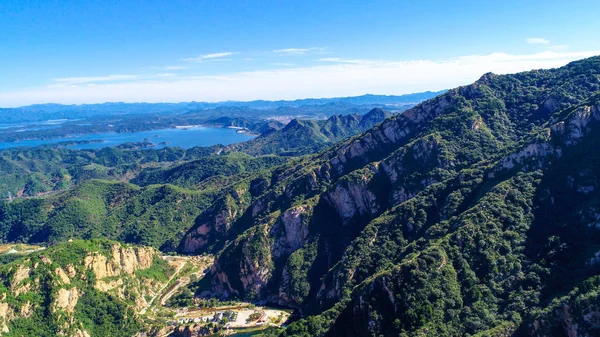 Aerial view of mountain with water reservoir  on the background. Mountain peak with beautiful blue sky and green forest. Landscape of mountain in natural reserve park. Miyun, Beijing, China.