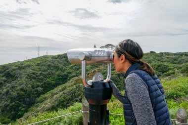 San Diego, Kaliforniya, ABD noktası Loma Yarımadası'nın uç üzerinde dürbün teleskop içinde arıyorsunuz Asya sportif kadın. San Diego şehir ve bay gözlemlemek için otomatik dürbün arayan genç kadın. işletilen sikke dürbün.