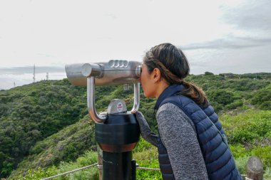 San Diego, Kaliforniya, ABD noktası Loma Yarımadası'nın uç üzerinde dürbün teleskop içinde arıyorsunuz Asya sportif kadın. San Diego şehir ve bay gözlemlemek için otomatik dürbün arayan genç kadın. işletilen sikke dürbün.