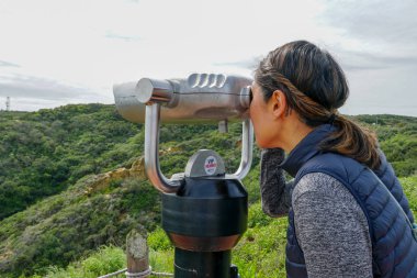 San Diego, Kaliforniya, ABD noktası Loma Yarımadası'nın uç üzerinde dürbün teleskop içinde arıyorsunuz Asya sportif kadın. San Diego şehir ve bay gözlemlemek için otomatik dürbün arayan genç kadın. işletilen sikke dürbün.