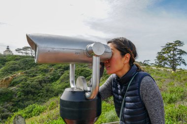 San Diego, Kaliforniya, ABD noktası Loma Yarımadası'nın uç üzerinde dürbün teleskop içinde arıyorsunuz Asya sportif kadın. San Diego şehir ve bay gözlemlemek için otomatik dürbün arayan genç kadın. işletilen sikke dürbün.