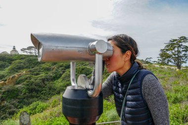 San Diego, Kaliforniya, ABD noktası Loma Yarımadası'nın uç üzerinde dürbün teleskop içinde arıyorsunuz Asya sportif kadın. San Diego şehir ve bay gözlemlemek için otomatik dürbün arayan genç kadın. işletilen sikke dürbün.