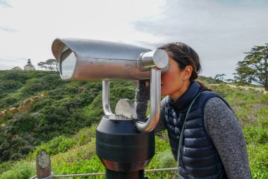 San Diego, Kaliforniya, ABD noktası Loma Yarımadası'nın uç üzerinde dürbün teleskop içinde arıyorsunuz Asya sportif kadın. San Diego şehir ve bay gözlemlemek için otomatik dürbün arayan genç kadın. işletilen sikke dürbün.