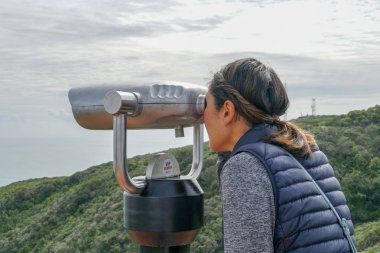 San Diego, Kaliforniya, ABD noktası Loma Yarımadası'nın uç üzerinde dürbün teleskop içinde arıyorsunuz Asya sportif kadın. San Diego şehir ve bay gözlemlemek için otomatik dürbün arayan genç kadın. işletilen sikke dürbün.
