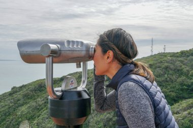 San Diego, Kaliforniya, ABD noktası Loma Yarımadası'nın uç üzerinde dürbün teleskop içinde arıyorsunuz Asya sportif kadın. San Diego şehir ve bay gözlemlemek için otomatik dürbün arayan genç kadın. işletilen sikke dürbün.