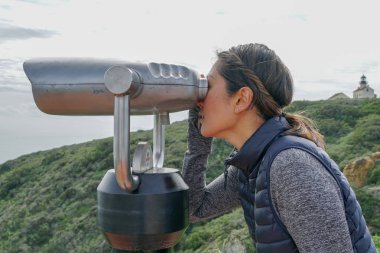 San Diego, Kaliforniya, ABD noktası Loma Yarımadası'nın uç üzerinde dürbün teleskop içinde arıyorsunuz Asya sportif kadın. San Diego şehir ve bay gözlemlemek için otomatik dürbün arayan genç kadın. işletilen sikke dürbün.