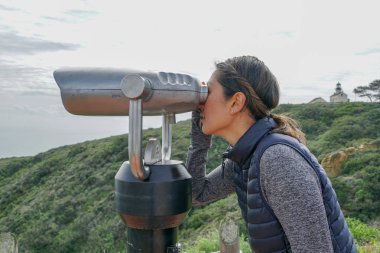 San Diego, Kaliforniya, ABD noktası Loma Yarımadası'nın uç üzerinde dürbün teleskop içinde arıyorsunuz Asya sportif kadın. San Diego şehir ve bay gözlemlemek için otomatik dürbün arayan genç kadın. işletilen sikke dürbün.