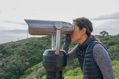 San Diego, Kaliforniya, ABD noktası Loma Yarımadası'nın uç üzerinde dürbün teleskop içinde arıyorsunuz Asya sportif kadın. San Diego şehir ve bay gözlemlemek için otomatik dürbün arayan genç kadın. işletilen sikke dürbün.