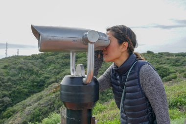 San Diego, Kaliforniya, ABD noktası Loma Yarımadası'nın uç üzerinde dürbün teleskop içinde arıyorsunuz Asya sportif kadın. San Diego şehir ve bay gözlemlemek için otomatik dürbün arayan genç kadın. işletilen sikke dürbün.