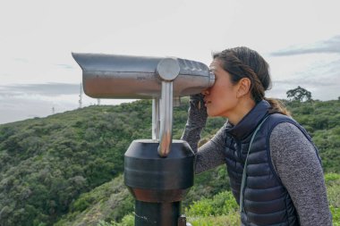 San Diego, Kaliforniya, ABD noktası Loma Yarımadası'nın uç üzerinde dürbün teleskop içinde arıyorsunuz Asya sportif kadın. San Diego şehir ve bay gözlemlemek için otomatik dürbün arayan genç kadın. işletilen sikke dürbün.