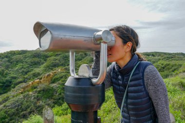 San Diego, Kaliforniya, ABD noktası Loma Yarımadası'nın uç üzerinde dürbün teleskop içinde arıyorsunuz Asya sportif kadın. San Diego şehir ve bay gözlemlemek için otomatik dürbün arayan genç kadın. işletilen sikke dürbün.