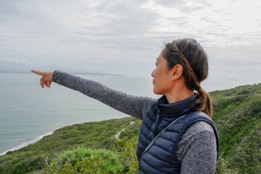 Genç sporcu Asyalı kadın güzel okyanus manzarasına bakıyor. Yürüyüş yapan genç bir kadın manzaraya hayran. sağlıklı aktif yaşam biçimi.
