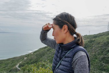 Genç sporcu Asyalı kadın güzel okyanus manzarasına bakıyor. Yürüyüş yapan genç bir kadın manzaraya hayran. sağlıklı aktif yaşam biçimi.